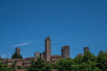 Fototapeta na wymiar San Gimignano town skyline and medieval towers on tne sky background. Trees in foreground. Tuscany, Italy, Europe. Summer, holiday, traveling concept.
