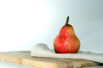 Red pear on a linen towel on the kitchen board. Light from the window