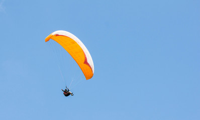 Paraglider waving his hand at the camera on an orange parachute on a bright day against a blue cloudless sky. Active lifestyle, extreme, healthy way to live.