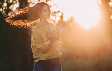Beautiful young girl, pretty woman in yellow shirt dancing in the light of the sun with a bouquet of lilac in her hand. Backlit image, bright, happiness, spring and heat and warmth. Women's Day.