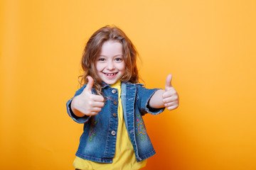 Cute little girl showing thumbs up on orange background