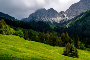 Fototapeta premium Alpine spring landscape with peaks covered by snow and clouds. View of idyllic mountain scenery in the Swiss Alps with fresh green meadows in a beautiful day in springtime.