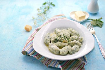 Gnocchi or dumplings with nettle or spinach on a white plate on a light blue background. Served with butter and parmesan cheese. Italian food. Selective focus