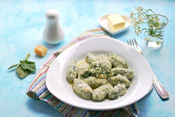 Gnocchi or dumplings with nettle or spinach on a white plate on a light blue background. Served with butter and parmesan cheese. Italian food. Selective focus