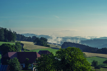 Naklejka premium Beautiful countryside mountain landscape with a village. Foggy sunset Germany, Black forest. Toned image. Sustainable ecosystem and healthy environment concept.