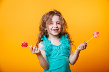 Funny child with candy lollipop, happy little girl eating big sugar lollipop on yellow bright...