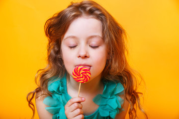 Beautiful little girl with sugar lollipop on yellow background