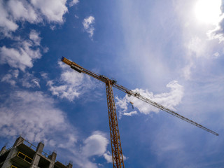 Crane on construction site, blue sky with white clouds background.