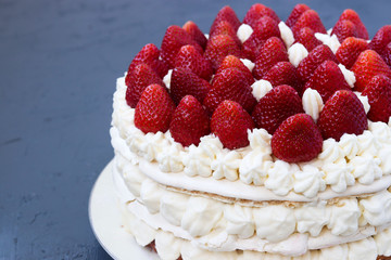 Cake Pavlova with strawberries and whipped cream, located on a dark background, horizontal