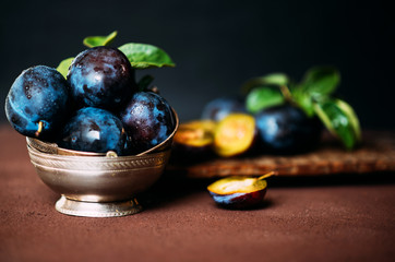 Garden plums on table. Close up of fresh plums with leaves. Summer or autumn harvest of plums. Toned image. Selective focus.