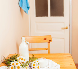 Simply stylish wooden kitchen with bottle of milk and glass on table, summer flowers camomile, healthy foog moring concept close up