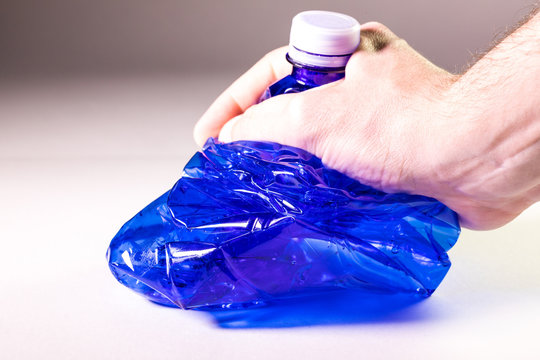Mano che sta schiacciando una bottiglia di plastica trasparente blu per la raccolta differenziata del multimateriale. Concetto di ecologia e stop all'inquinamento.