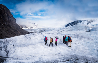 Back view of professional mountaineers in warm clothes walking on icy surface glacier by snowy mountain in Iceland