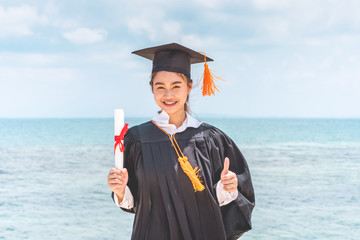 Graduated woman in cap and gown holding certificated celebrating in Commencement day with blue sky...