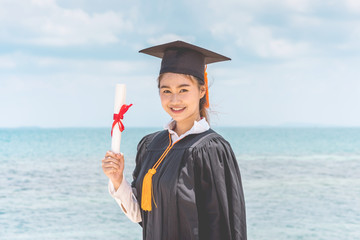 Graduated woman in cap and gown holding certificated celebrating in Commencement day with blue sky...