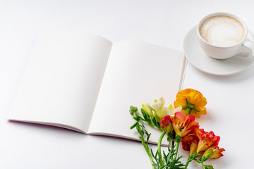 Flatlay with freesia flowers, capuccino cup and opened notebook on white background