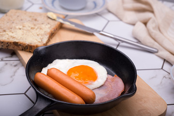 breakfast in pan with fried eggs, sausages, bacon, toasts and coffee