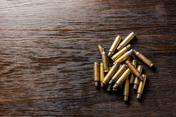 Empty bullet casings on a dark, wooden table. - obrazy, fototapety, plakaty