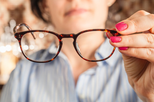 female hand holding a brown framed glasses