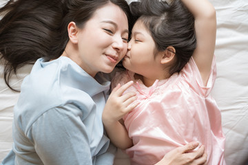 Daughter kisses her mother's cheek. and hugging in the bedroom .Happy Asian family