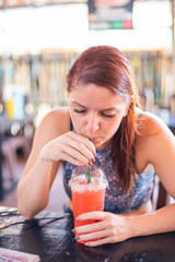 Portrait of a beautiful and cheerful redhead woman with wet hair drinking a refreshing cocktail in a street cafe. Girl on vacation drinks a cocktail after swimming