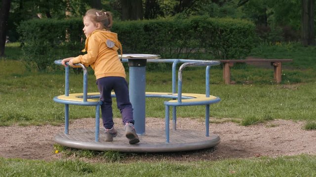 Funny little kid girl play in a park playground fail falling during spinning the carousel trying to jump on it