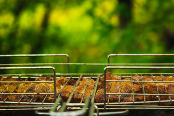 cubes of pickled meat in a grill grate at brazier. barbecue kebab on embers outdors. grilled picnic in nature. side view close up a background of green trees