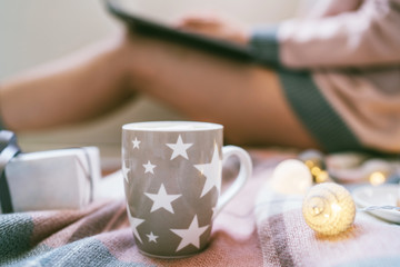 Winter hot drinks. Close up cup of coffee or hot chocolate. Blurred image womam in warm pink sweater with laptop, home comfort and relax. Christmas holidays, hot drinks and people concept.