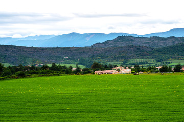 Fototapeta na wymiar Picturesque rural landscape. Countryside of France with fresh green field, small village and mountain landscape in the background. Eco tourism.