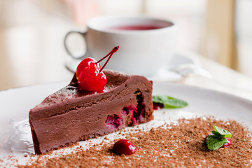 A cup of tea with a chocolate brownie cake with cherries and mint. Sweet сhocolate dessert in a...