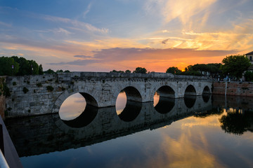 Famous place in Rimini, Italy. Beautiful sunset over the Tiberius Bridge, with reflection in the river.