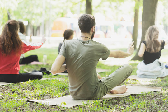Beautiful happy people wearing trendy business uniform while making yoga in park