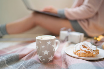 Winter hot drinks. Close up cup of coffee or hot chocolate. Blurred image womam in warm pink sweater with laptop, home comfort and relax. Christmas holidays, hot drinks and people concept.
