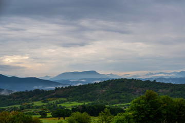 Fototapeta premium Picturesque rural landscape. Countryside of France with fresh green forest and meadow. Mountain landscape in the background. Beautiful day after a summer thunderstorm with a cloudy sky. Eco tourism.