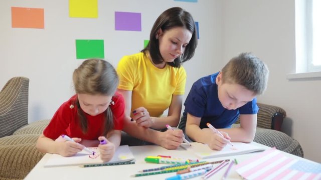 A caring mother teaches two of her children to draw the flag of America with colored pencils and felt-tip pens for America’s Independence Day.