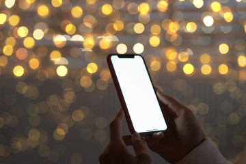 Smart phone showing blank screen in woman hand at street on the Christmas lights blured background.