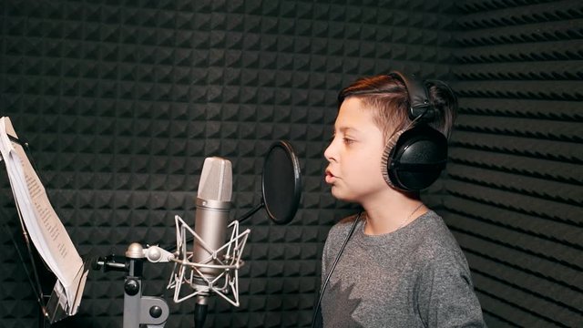 A boy is recording a song in a recording studio. The boy in the headphones.