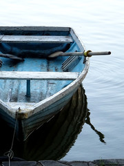 A traditional wooden boat tied on shore of a lake in the evening at sunset.Lonely fishing boat in the blue water on a peaceful day. The oars used in rowing are attached to the boat being rowed.   