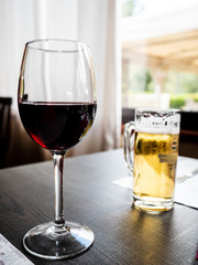 glass of red wine at restaurant on wooden table, in the background a mug of beer