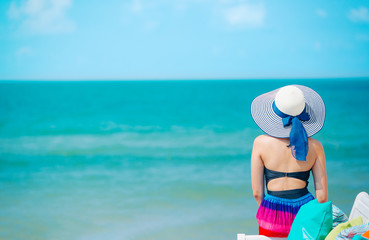 Fototapeta na wymiar Woman enjoying beach relaxing joyful in summer by tropical blue water. Bikini model on travel wearing beach hat.