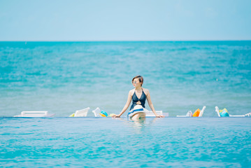 Woman enjoying beach relaxing joyful in summer by tropical blue water. Bikini model on travel wearing beach hat.