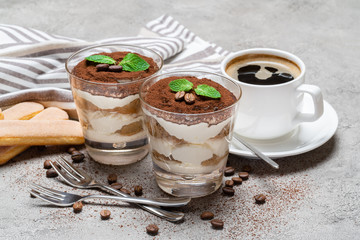 two portions Classic tiramisu dessert in a glass and cup of coffee on concrete background