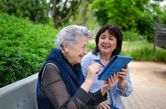 Cheerful female carer shows how to use the tablet and a senior woman gladly repeats