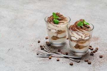 two portions Classic tiramisu dessert in a glass on concrete background