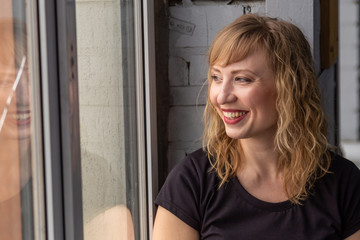 A woman of 30 years with blond hair near the window, you can see her reflection