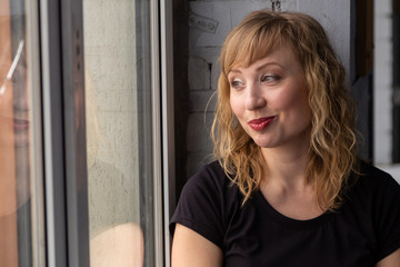 A woman of 30 years with blond hair near the window, you can see her reflection