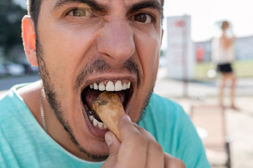 A young man eats black ice cream in a cone. Because of the black ice cream, his whole face and teeth are black.