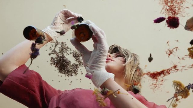 Young woman perfumer preparing herbs and flowers for make a perfume. Under table view.