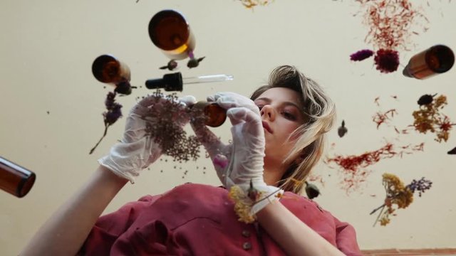 Young woman perfumer preparing herbs and flowers for make a perfume. Under table view.