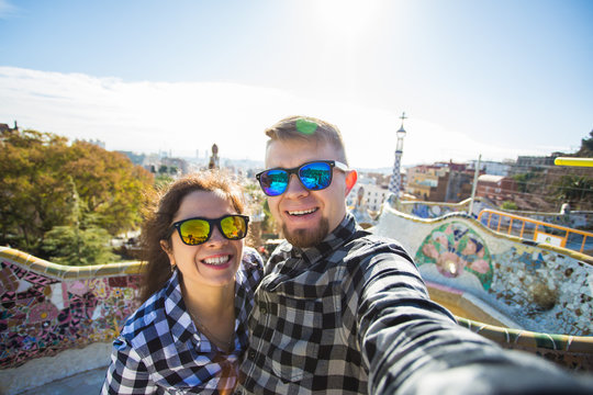 Funny young couple looking at camera taking photo with smart phone smiling in Park Guell, Barcelona, Spain.